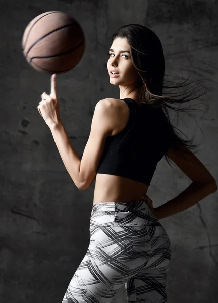 Jogador de basquete mulher girando bola no dedo na parede do sótão de concreto — Fotografia de Stock