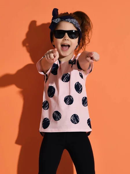 Kız çocuk Yaz gömlek ve turuncu zemin üzerine parmakları işaret güneş gözlüğü poz — Stok fotoğraf