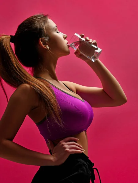 Krásný sport žena pitnou vodu ze skla na růžovém pozadí — Stock fotografie