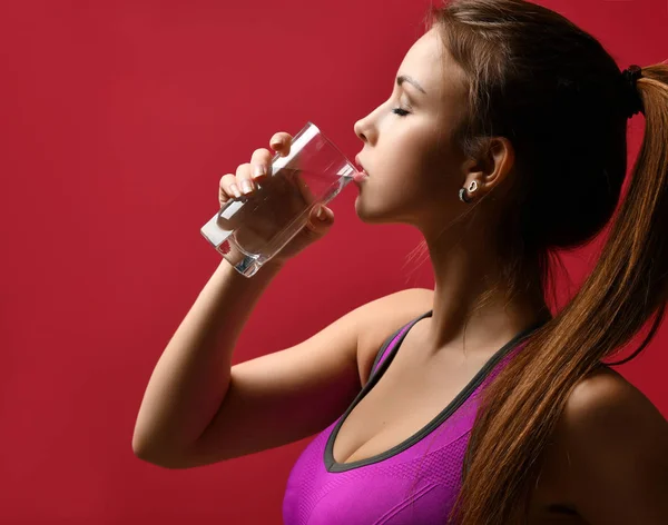 Beautiful sport woman drinking water from glass on pink background — Stock Photo, Image