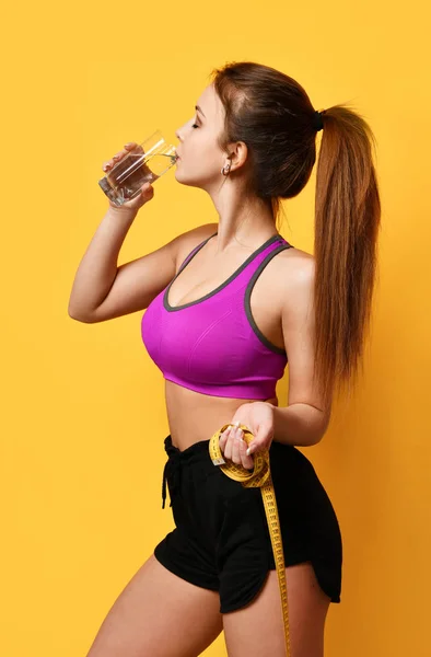 Hermosa mujer del deporte mantenga cinta métrica y agua potable de vidrio sobre fondo amarillo —  Fotos de Stock