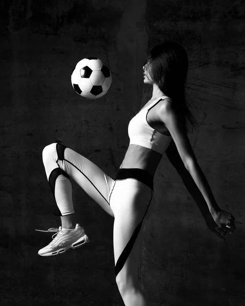 Soccer woman player jumps and hit the ball strike in the middle on concrete loft wall background. Black and white image