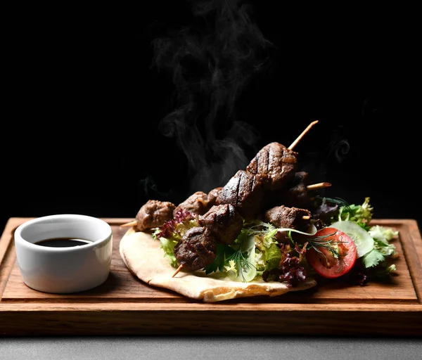 Tasty barbecue beef shashlik on wood plate with fresh vegetables and steam smoke — Stock Photo, Image