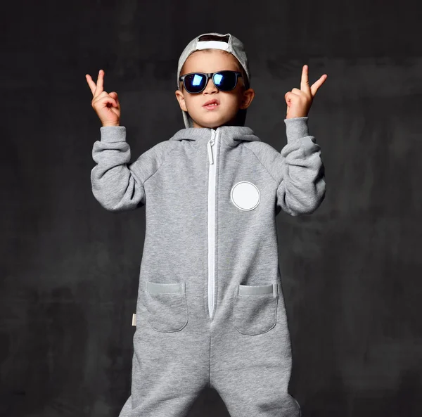 Niño en traje gris sombrero y gafas de sol muestran signo de paz en la oscuridad —  Fotos de Stock