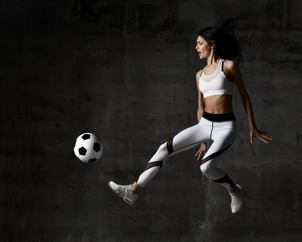 Piłkarz kobieta skacze i uderzył piłkę strajku w środku na mur beton loft — Zdjęcie stockowe