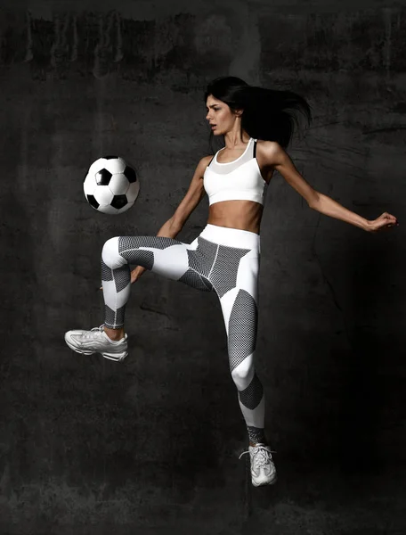 Futebol jogador mulher salta e acertar a bola greve no meio na parede do sótão de concreto — Fotografia de Stock