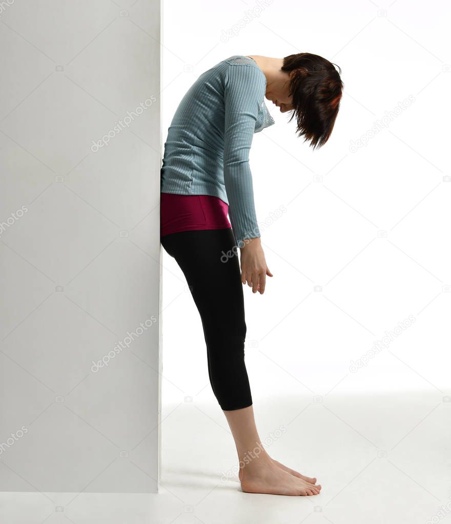 Woman exercising doing postnatal workout. Female fitness instructor stretching her spine near wall in gym work out exercises