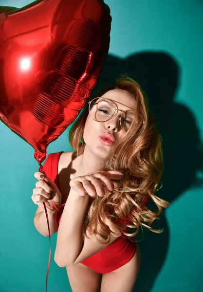 Όμορφα σγουρά μαλλιά νεαρή γυναίκα σε σαφή γυαλιά aviator κατέχουν μεγάλο μπαλόνι κόκκινο αστέρι σημάδι φιλί χτύπημα με τα χείλη στο Νομισματοκοπείο φόντο — Φωτογραφία Αρχείου