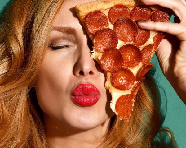 Donna tenere grande fetta di peperoni pizza fetta colpo baciare segno su sfondo blu menta — Foto Stock