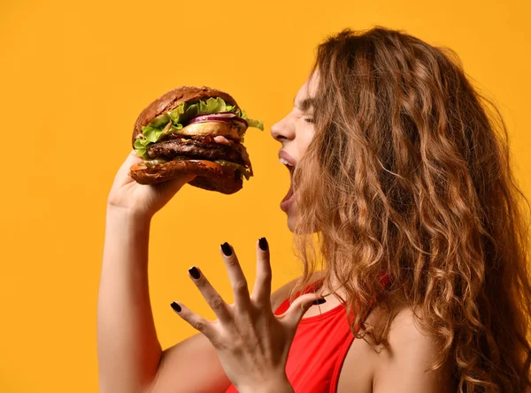 Kobieta jeść kanapkę burger z usta głodny na żółtym tle — Zdjęcie stockowe