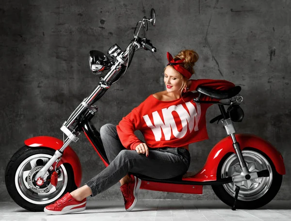 Donna cavalcare nuova auto elettrica moto scooter presente per il nuovo anno 2019 in camicetta rossa e jeans su sfondo muro di cemento — Foto Stock