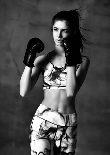 Jeune sport femme boîte entraîneur boxe en gants noirs sur mur loft en béton noir et blanc image — Photo