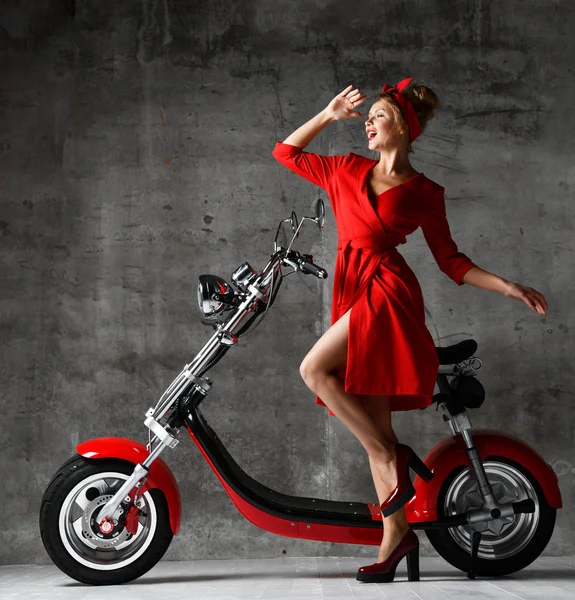 Donna cavalcare nuova auto elettrica moto scooter presente per il nuovo anno 2019 in camicetta rossa e jeans su sfondo muro di cemento — Foto Stock