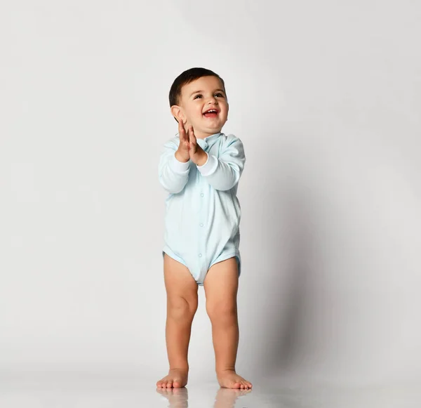 Niño bebé niño niño niño en tela de cuerpo azul claro dar los primeros pasos en gris —  Fotos de Stock