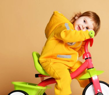 Bebek kız çocuk üzerinde açık gri ararken sıcak sarı tulum onun ilk bisiklet bisiklet sürme 