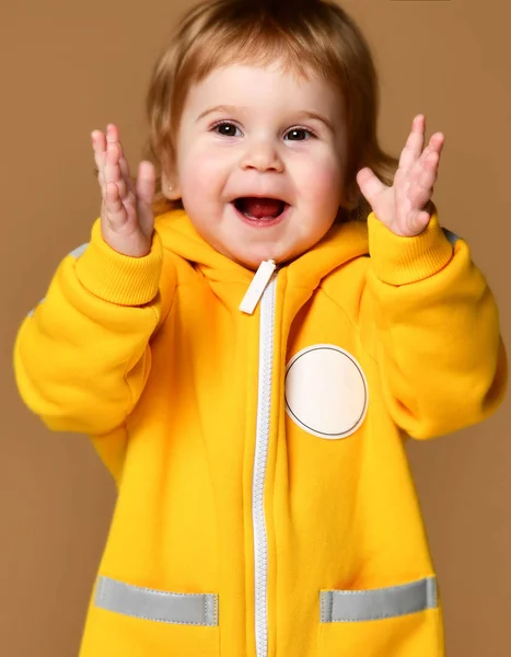 Kind kind baby meisje kind peuter in winter gele Amerikaanse overalls clap haar handen gelukkig lachend op brown — Stockfoto