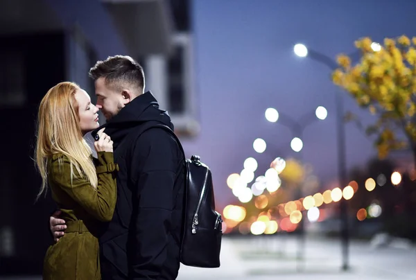 Молодая пара, идущая по вечерней улице, улыбающаяся, целующаяся в городе — стоковое фото