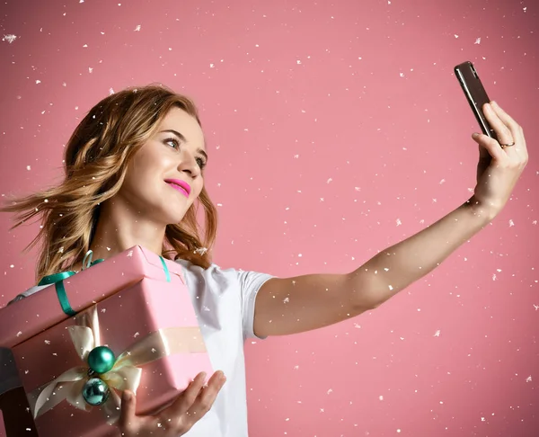 Genç güzel kadın Noel hediye hediyeler gülümseyen tutun ve selfie fotoğraf ile cep telefonunu Mobil olun — Stok fotoğraf