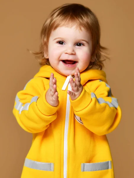 Kind kind baby meisje kind peuter in winter gele Amerikaanse overalls clap haar handen gelukkig lachend op brown — Stockfoto