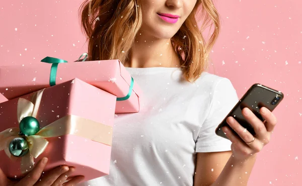 Mobil cep telefonu ile Noel için alışveriş online kadın pembe üzerinde gülümseyen hediyeler sunar — Stok fotoğraf