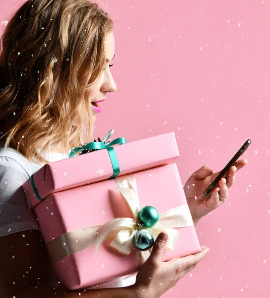 Donna shopping online con cellulare per Natale presenta regali sorridenti su rosa chiaro — Foto Stock
