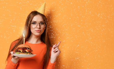 Kadın tutun büyük mermer etli çizburger sandviç pastel sarı arka plan üzerinde mum yanan ile Doğum günü partisi için