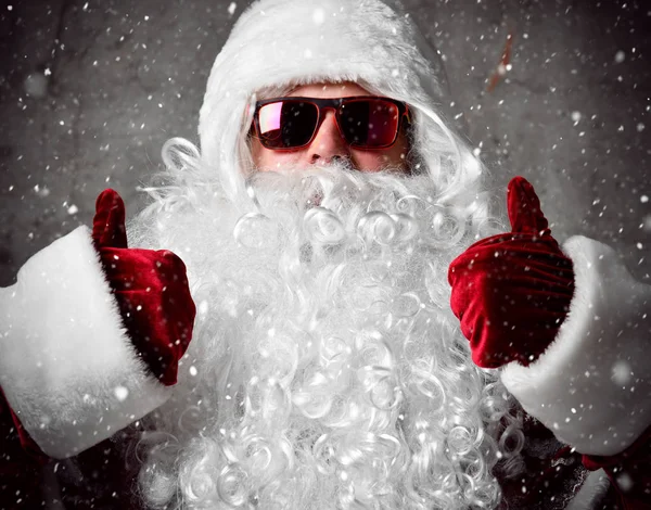 Santa Claus δείξει τους αντίχειρες κάτω από το χιόνι κομφετί. Το νέο έτος και καλά Χριστούγεννα — Φωτογραφία Αρχείου