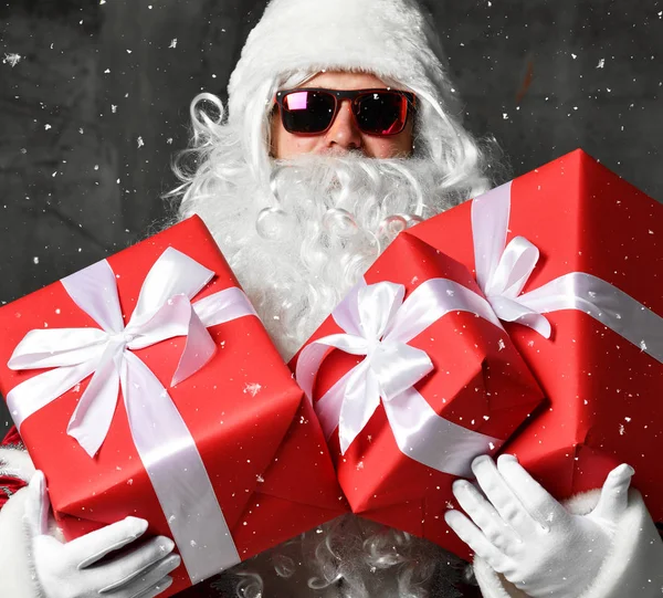 Santa Claus con regalos rojos para el año nuevo y gafas de sol bajo la nieve —  Fotos de Stock