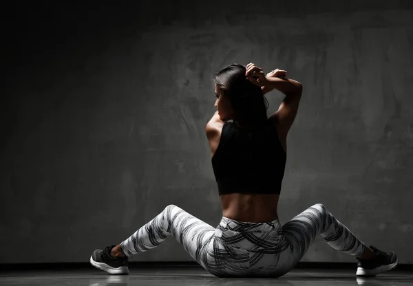 Jonge sport vrouw in training oefening doek poseren zitten uitrekken zich splitst in de sportschool op donkergrijs — Stockfoto