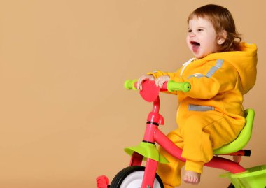 Bebek kız çocuk üzerinde açık gri ararken sıcak sarı tulum onun ilk bisiklet bisiklet sürme 