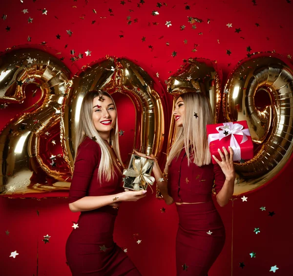 Twee vrouwen vieren op Nieuwjaar partij gelukkig lachen meisjes in casual jurken gooien gouden sterren confetti met 2019 ballonnen — Stockfoto