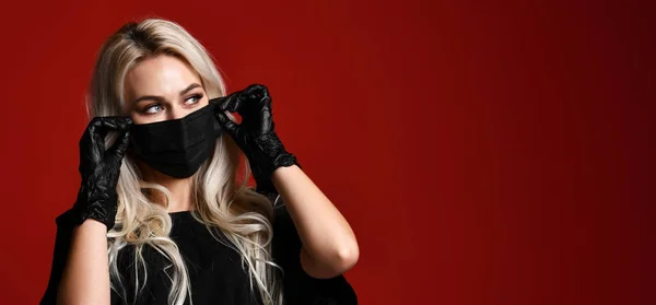 Mulher bonita em máscara médica preta protetora e luvas em fundo vermelho escuro — Fotografia de Stock