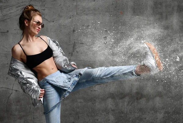 Молода спортивна жінка штовхає пилові снігові бризки з вправами ноги стоїть в срібному сексуальному тонкому пуховику — стокове фото