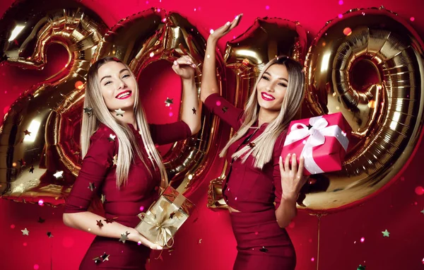 Twee vrouwen vieren op Nieuwjaar partij gelukkig lachen meisjes in casual jurken gooien gouden sterren confetti met 2019 ballonnen — Stockfoto