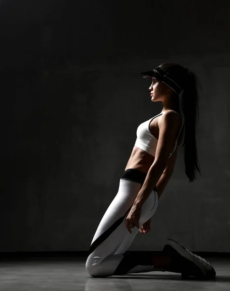 Joven mujer deportiva en ejercicio ejercicio de tela posando estiramiento en el gimnasio sobre fondo gris oscuro — Foto de Stock