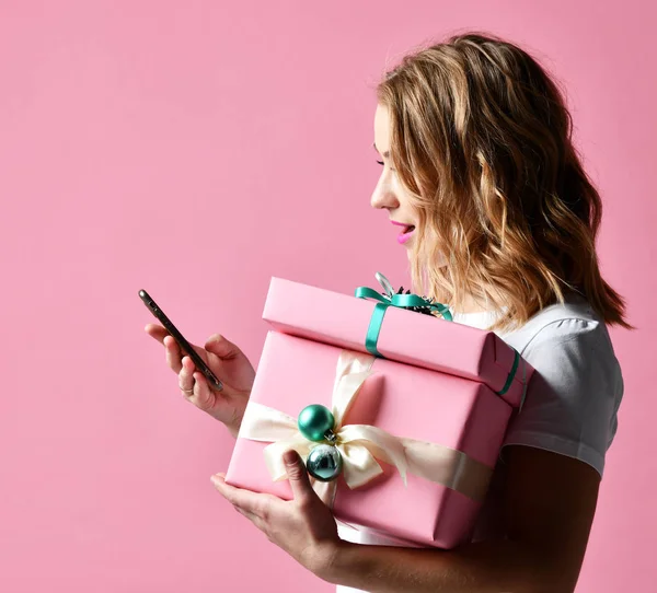 Donna shopping online con cellulare per Natale presenta regali sorridenti su rosa chiaro — Foto Stock