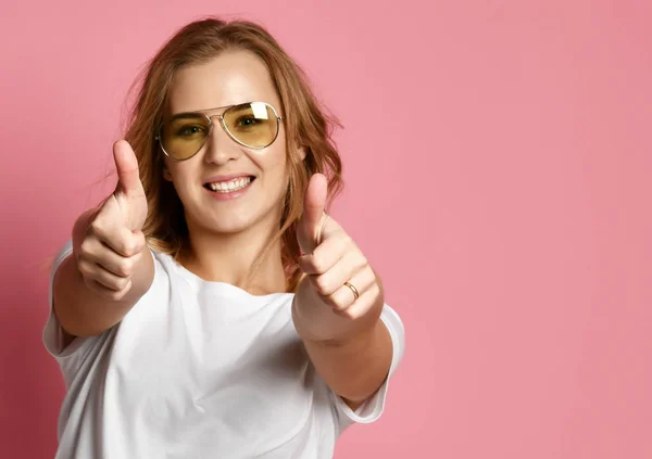 Beautiful woman in white t-shirt and aviator sunglasses show thumbs up sign on pink — Stock Photo, Image