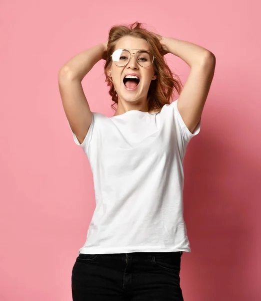 Mulher em t-shirt branca e óculos modernos posando gritando com as mãos para cima em rosa — Fotografia de Stock