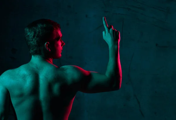 Neonlicht-Porträt eines sexy lächelnden, muskulösen Mannes, der in die Ecke blickt und mit dem Finger nach oben zeigt — Stockfoto