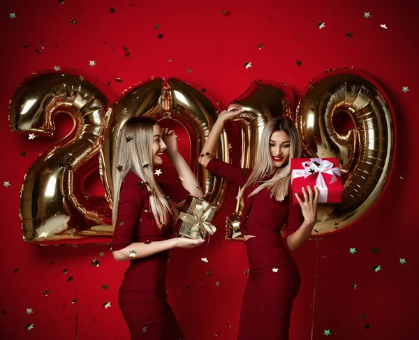 Twee vrouwen vieren op Nieuwjaar partij gelukkig lachen meisjes in casual jurken gooien gouden sterren confetti met 2019 ballonnen — Stockfoto