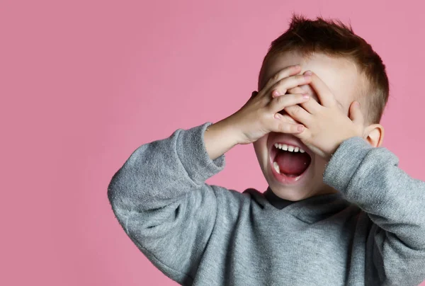 Bebé niño cubriendo cerrar los ojos con las manos y las palmas gritando riendo sobre rosa —  Fotos de Stock
