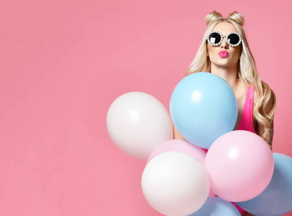 Blonde woman on birthday party having fun with pastel color air balloons blow kiss in round sunglasses — Stock Photo, Image