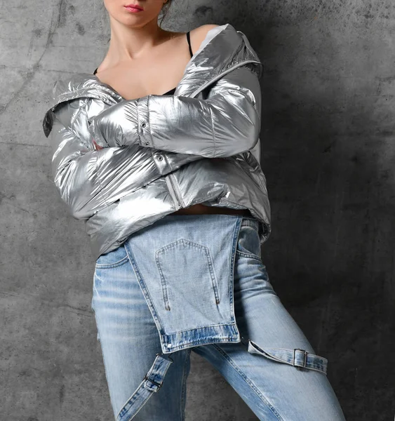 Sportovní žena v modrých džínách Silver tenký dole puffer jacket stojící na zeď loft — Stock fotografie