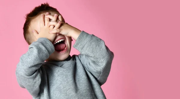 Bebé niño cubriendo cerrar los ojos con las manos y las palmas gritando riendo sobre rosa — Foto de Stock
