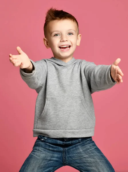 Młody chłopak dziecko w szara Bluza z kapturem, wskazując palcem na rogu uśmiechający się na różowym tle — Zdjęcie stockowe