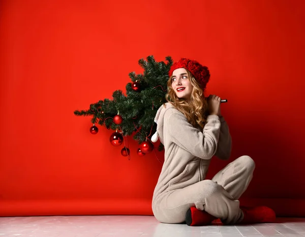 Mladá žena drží zimní vánoční jedle strom dekorace v pletené čepici pod sněhem. Nový rok koncepce — Stock fotografie