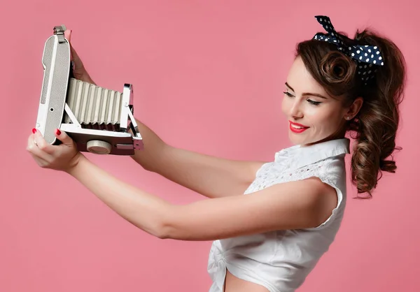 Fiatal pinup stílusú nő veszi használatát antik régi hordozható fénykép fényképezőgép közepes képkeret világos rózsaszín — Stock Fotó