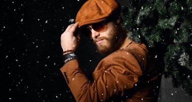 Kahverengi deri ceket ve kap sakallı adam tutun Noel ağacı altında kar
