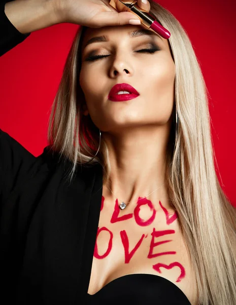 Beautiful sexy young woman makeup artist hold red lipstick rouge with love heart text on body on red — Stock Photo, Image