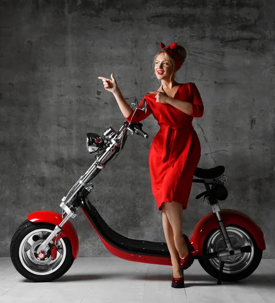 Woman ride sit on motorcycle bicycle scooter pinup retro style pointing finger laughing smiling red dress